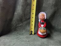 Front view of the figurine, showing the overall shape, color, and size next to a measuring tape indicating approximately 6.5 inches tall.