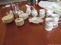 Wide view photo showing an assortment of small bowls, mugs, and serving pieces on a wooden surface