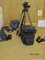 Full view of lot including the three cameras, tripod, batteries, and carrying bags arranged on carpet indoors.