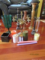 Wide view of assorted candle holders and candles arranged on a wood surface including wood, glass, brass, and ceramic items with various candles.