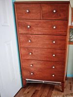Front view of wooden chest of drawers with six drawers and metal knobs on wooden legs with metal base.