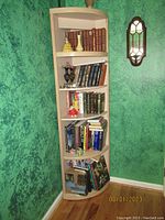 Photo of wooden corner shelf in a green-walled room showing five shelves filled with books and decorative items.