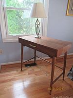 Wooden desk angled view showing the single drawer and tapered legs with brass handle.