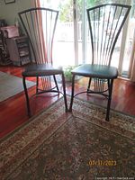 Front view of two metal dining chairs showing curved vertical rod backrests and black cushioned seats.