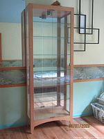 Full view of the tall glass display cabinet with wood frame against blue wall, showing four glass shelves and mirror back