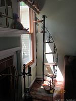 Full view of the 7-tier wrought iron and wood display shelf near a window showing its spiral design and decorative wrought iron details.