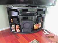 Black wood entertainment cabinet under TV with curved open shelves and electronic devices, showing size and shape.