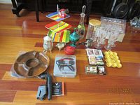 Photo showing 3-tier striped serving tray, vintage beer glasses, glass decanter, wooden platter, 2 wine openers (Houdini and Coravin), Le Creuset pot, egg dish, plastic flutes, and small tins arranged on floor