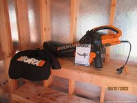 Worx WG500 blower with collection bag and user manual, orange and black handheld device