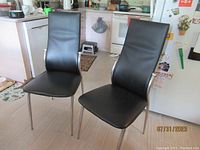 Front view of two black faux leather GEM dining chairs with chrome legs, placed side by side in kitchen area.