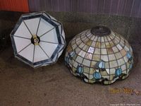 Photo showing both the 15-inch diameter stained glass hanging light fixture and the large stained glass lamp shade side by side on a counter.