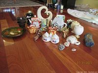 Overview of assorted kitchen items laid out on wooden floor including vintage plate, salt and pepper shakers, sugar and creamer set, bowls, teapots and small figurines.
