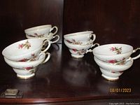 Eight floral luncheon cups arranged in two stacks on a shelf, showing gold accents on rims and handles.