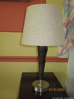 Mid century style table lamp showing wooden twisted cone base with metal bottom plate and beige fabric shade.