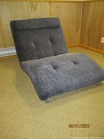 Front and side angled view of oversized double sofa chair showing tufted upholstery, black textured fabric, angled backrest, and caster wheels.