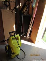 Front view of yellow Karcher power washer with hose coiled on back and spray gun attached