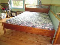 Full view of the queen size bed showing solid wood frame, floral patterned mattress, headboard and footboard.