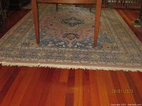 Photo showing the full length of the oriental style rug under a wooden table on hardwood floor, highlighting the fringe and border.