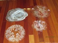 Four vintage glass serving pieces on wooden floor: two pink floral embossed Mikasa Rosella pieces and two frosted embossed glass platters (fruit autumn cake plate and large platter).