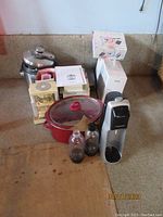 Wide view showing most items: Rival slow cooker, Proctor Silex slow cooker, George Foreman grill, red stoneware pot with glass lid, SodaStream with bottles, meat tenderizer, instruction manuals.