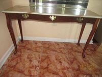 Full view of the dark brown wooden console table with a faux drawer and decorative brass handles, placed against a wall with tile flooring.