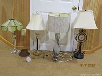 Full view of four vintage table lamps and one clamp lamp lined up on floor against wall.