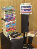 Stack of 20 Walt Disney VHS tapes with colorful covers, including some cases and a tape out of case, along with 3 empty cases and 7 additional children's VHS movies