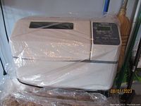 Zojirushi bread maker unit covered in plastic wrap showing overall condition and design.