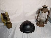 Full lot view showing gas mask, metal helmet and lantern together against white background indicating size and relative condition.