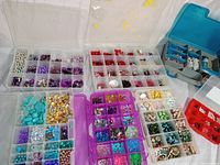 Overhead view of several open plastic containers filled with a variety of semi-precious stones and beads sorted by color and type