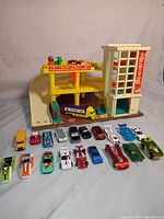 Front view showing the parking garage and 17 toy cars lined up in front in multiple colors and styles