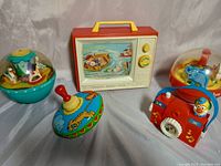 Photo showing the complete lot of toys positioned on a cloth background including the TV toy, two dome chime balls, metal spinning top, and clown camera music box toy.