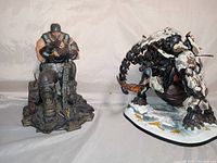 Two statues side by side on a light surface: Marcus Fenix holding a gun on a base and the mechanical Elephant Tremortusk crouched on a round base.