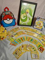 Wide view of the Pokémon lot showing cards laid out in rows, the signed Snivey poster in a black frame, Pikachu plush, Poké Ball backpack, and the sealed Diamond & Pearl game box.