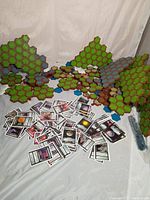 Wide view of multiple Heroscape green, brown, and grey hexagonal land pieces arranged upright and flat with scattered Star Trek cards in front.