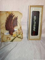 Photo showing painted quartz slice with eagle and framed jade zodiac animal string side by side on a light surface.