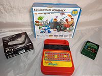 Photo showing the entire lot: PlayStation multi tap box, Speak & Spell, Legends Flashback box, and Football 2 game.