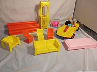Photo showing yellow and orange Barbie townhouse parts including orange columns, yellow elevator post, various chairs, pink table, yellow and pink swing, 1979 Barbie yellow Corvette with dolls seated