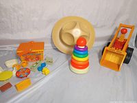 Photo of all items including Tonka safari hat, Fisher Price stacking rings, push shovel digger tractor, picnic basket and miniature furniture/toys spread out on white cloth background