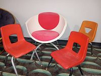 One white and red Ikea Gubbo swivel chair and three mid-century child's stacking chairs in red and orange colors arranged on a patterned carpeted floor.