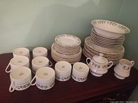 Full set arranged showing stacked dinner plates, small plates, bowls, tea cups, saucers, creamer, and sugar pot all featuring festive Mistletoe design.