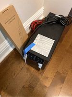 Photo of UPS backup battery and boxed 6 outlet surge protector with USB charger on floor.