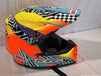 Side view of helmet showing vibrant color scheme and Bell logos on side and visor, with checkered details and Tagger Designs branding