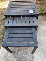 Three black metal square slat top side tables shown stacked and arranged on concrete next to grass. Tables have visible wear and surface rust spots consistent with outdoor use.