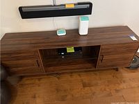 Full view of the dark walnut media console with some objects placed on top and central compartment containing electronic device.