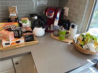 Red Keurig coffee maker on countertop with white kettle, wooden tray and various coffee and tea items spread out