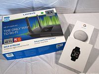 Photo showing unopened Linksys router box, Google Nest Mini box, and smart watch box together