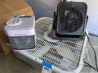 Lot showing the Arctic Air evaporative cooler and one black small box fan, with cords visible, placed on a metal rack.