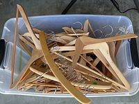Top view of a large plastic bin filled with assorted wooden hangers with metal hooks and clips.