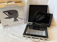 Neewer X12 teleprompter in open metal carrying case, showing the teleprompter glass and box with product image.